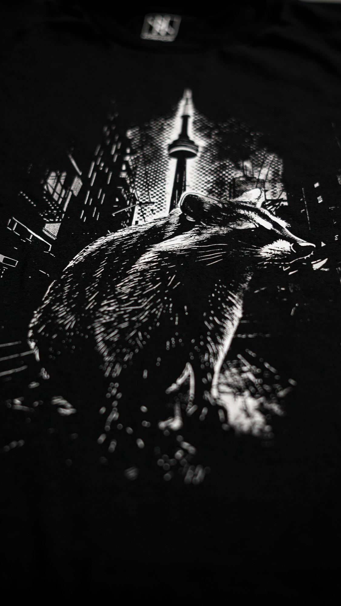 close-up of the Noir et Noir Toronto Urban Raccoon T-shirt, showcasing the intricate details of the black-on-black raccoon print and the gold lettering that says 'Toronto.' Highlights the premium craftsmanship and attention to detai
