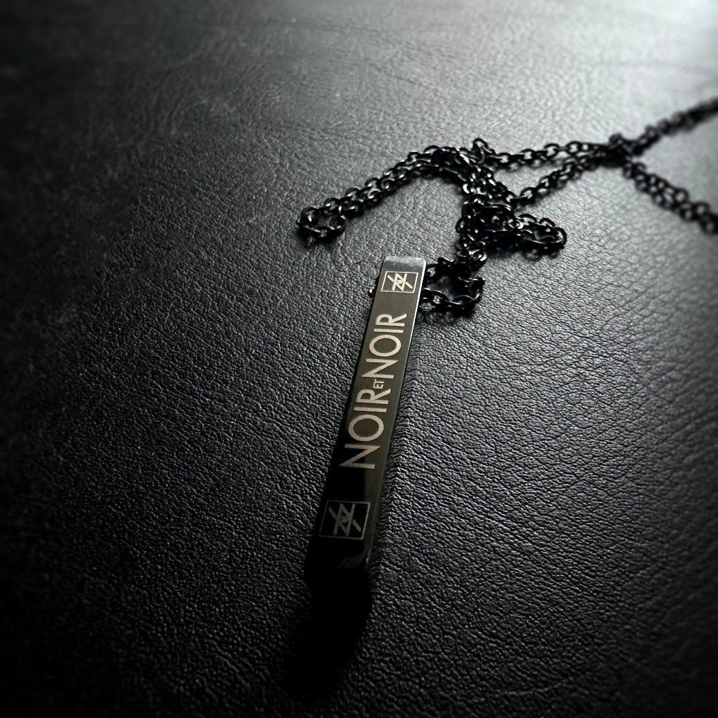 Noir et Noir Rectangular Minimalist Stainless Steel Bar Pendant necklace on dark textured surface with chain.