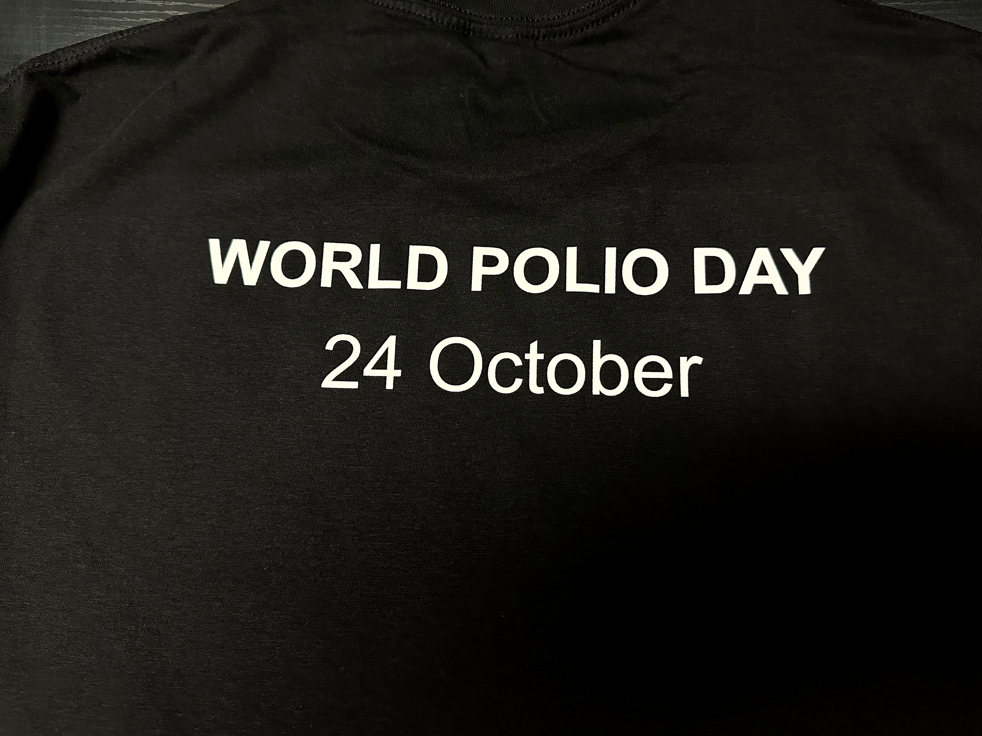 World Polio Day T-shirt in black with white text reading "WORLD POLIO DAY 24 October" celebrating polio survivors.