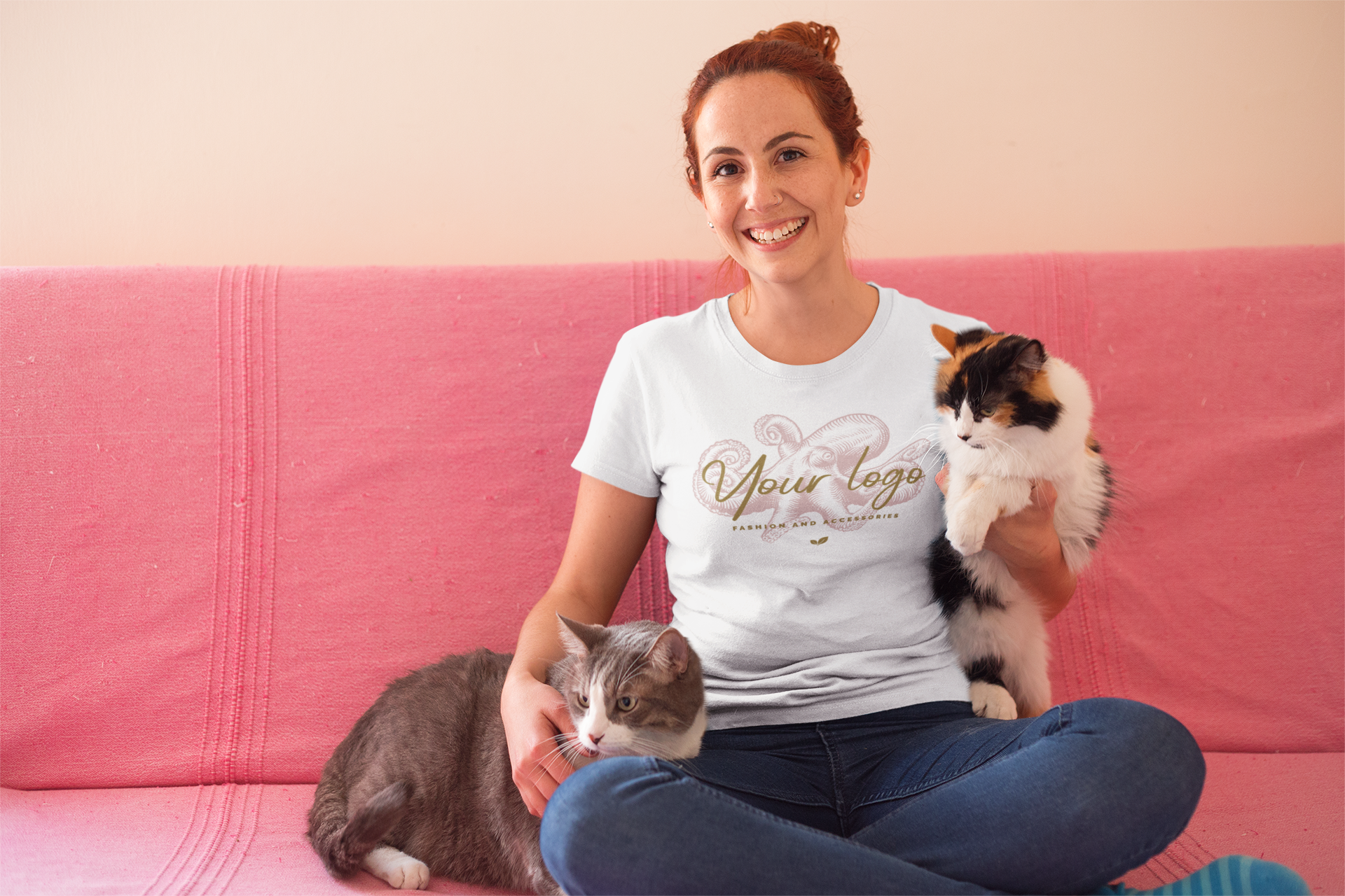 Woman wearing Women's Fit Softstyle 100% Cotton Tee sitting on pink couch holding two cats.