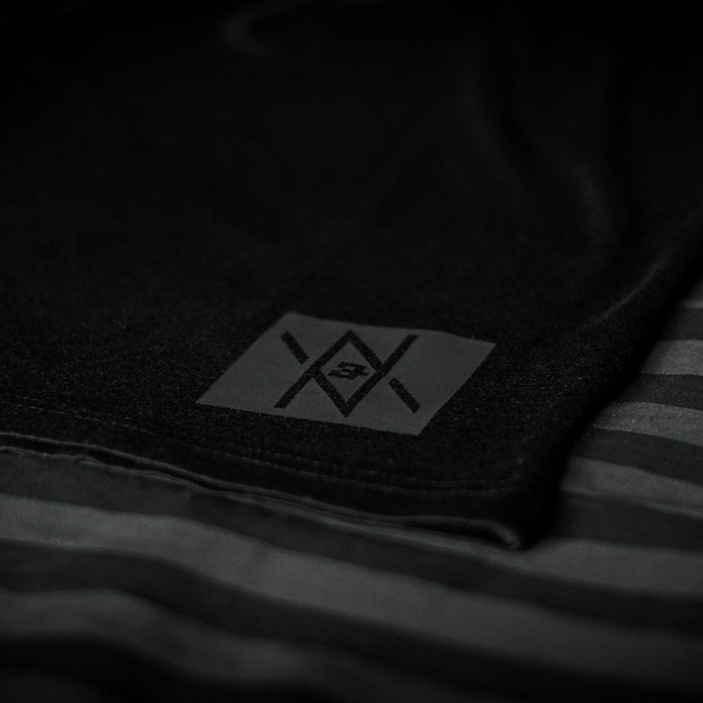 Detailed view of the Noir et Noir Feathered Snake unisex T-shirt's black-on-black logo, highlighting the precision and quality of the print. Essential for a modern, minimalist wardrobe. Featured in the Design Collection.