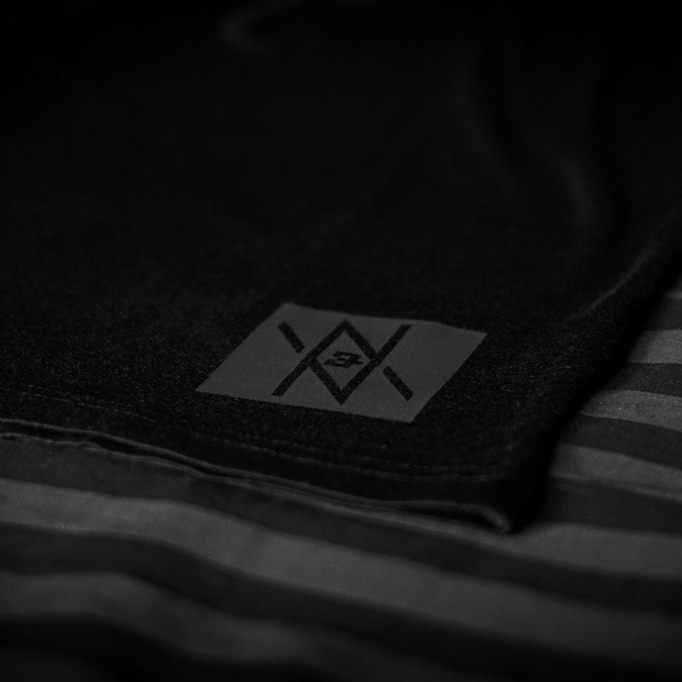 Detailed view of the Noir et Noir Raven unisex T-shirt's black-on-black logo, highlighting the precision and quality of the print. Essential for a modern, minimalist wardrobe. Featured in the Design Collection.