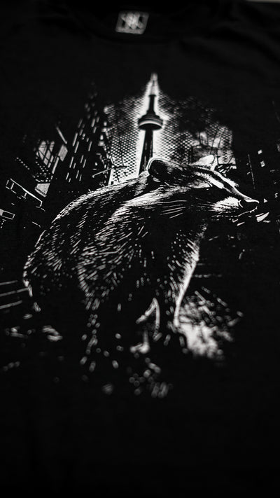 close-up of the Noir et Noir Toronto Urban Raccoon T-shirt, showcasing the intricate details of the black-on-black raccoon print and the gold lettering that says 'Toronto.' Highlights the premium craftsmanship and attention to detai